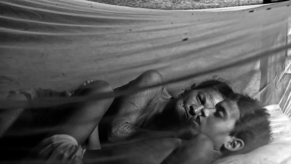 Al Oeste, en Zapata (2025) | Análisis audiovisual del documental de David Bim | CineFilm Fotograma en blanco y negro de “Al oeste en Zapata”: mujer y niño descansando bajo una mosquitera, reflejando intimidad, pobreza y contexto rural.