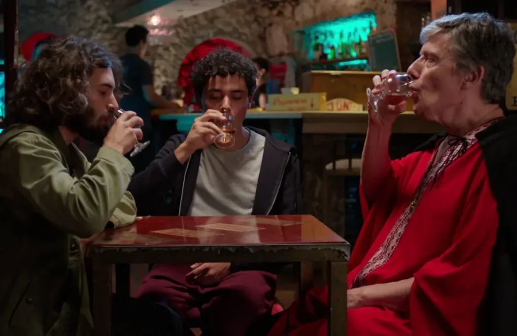 Escena de Arvore do Conhecimento (2025) con tres personajes sentados en un bar bebiendo en una mesa.