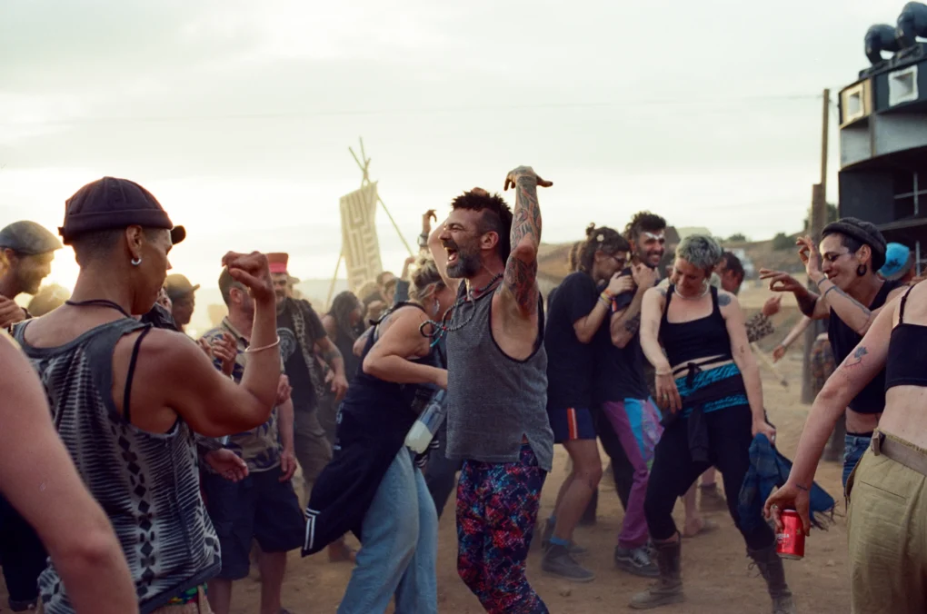 Escena de baile colectivo al aire libre en la película Sirat (2025), con grupo de personas celebrando al atardecer.