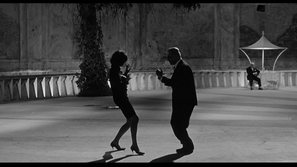 Fotograma de 8½ de Federico Fellini con dos figuras bailando en un espacio abierto.
