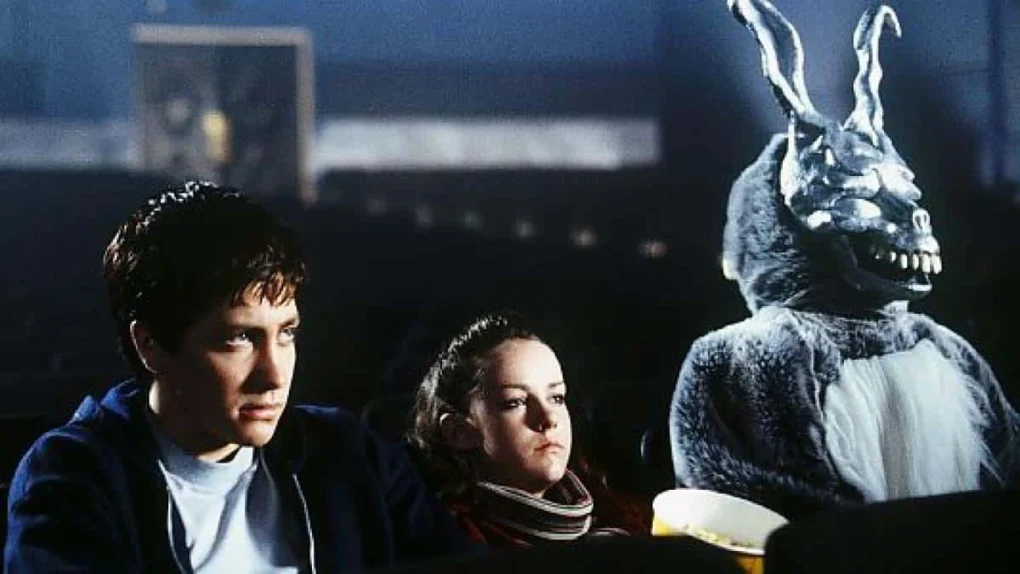 Fotograma de Donnie Darko con dos adolescentes sentados junto a una figura disfrazada de conejo.