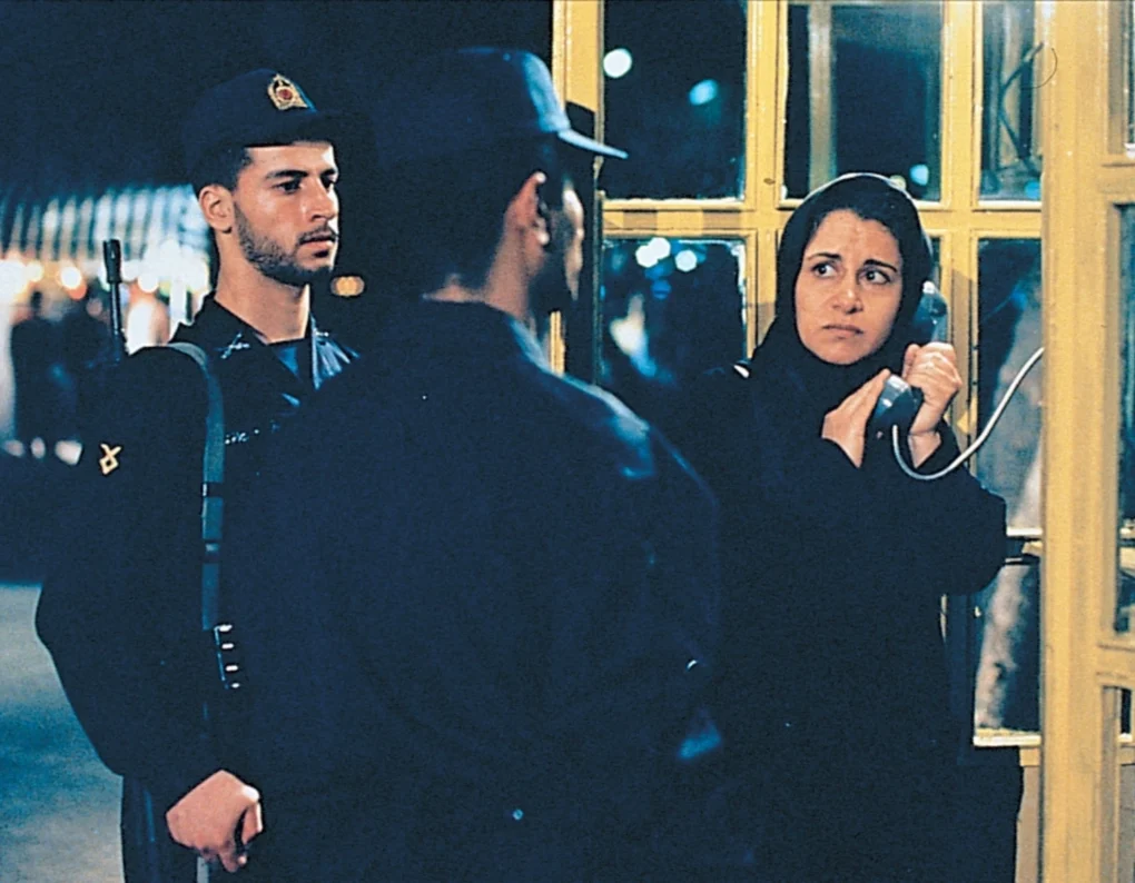 Mujer vigilada por policías usando teléfono en El círculo (2000) de Jafar Panahi