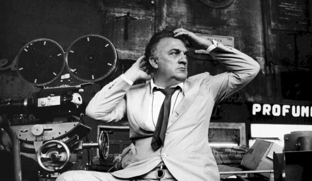 Federico Fellini posa junto a una cámara de cine en una fotografía en blanco y negro.