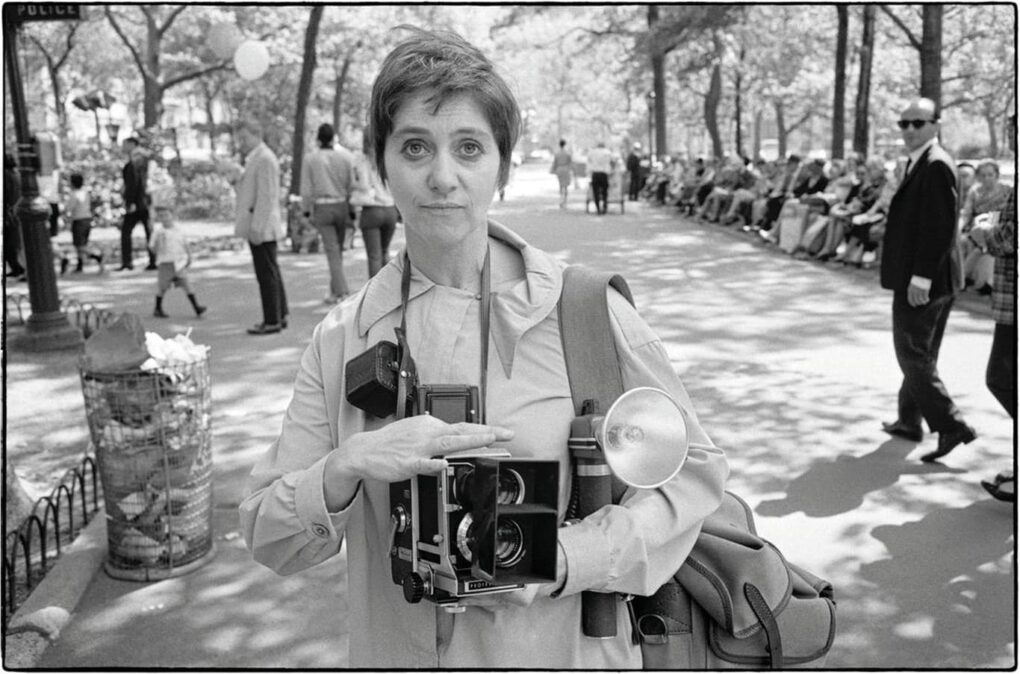 Diane Arbus sostiene una cámara en un retrato en blanco y negro al aire libre.