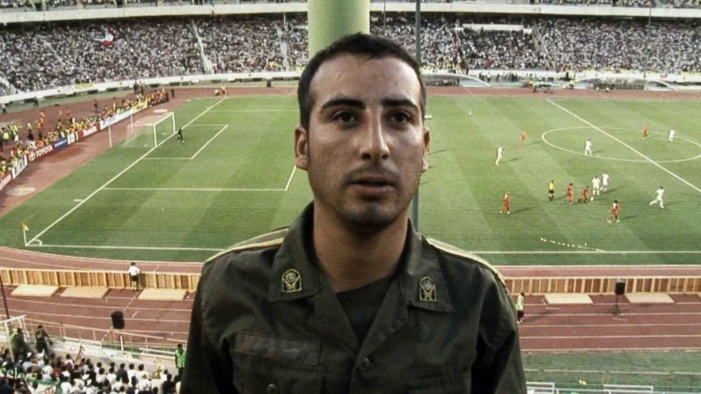 Fotograma de Offside (Fuera de juego) de Jafar Panahi con un soldado en el estadio durante un partido de fútbol.