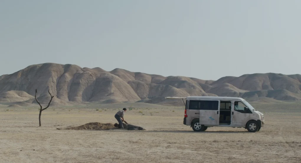 Plano del desierto con una furgoneta y una figura junto a una zanja en Un simple accidente (2025), de Jafar Panahi