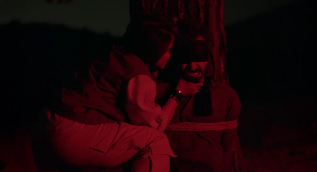 Escena nocturna iluminada en rojo con una mujer y un hombre atado en Un simple accidente (2025), de Jafar Panahi
